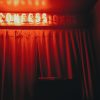 photo of a red curtain with a neon sign saying "confession" with only "confess" lit up