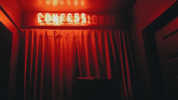 photo of a red curtain with a neon sign saying "confession" with only "confess" lit up