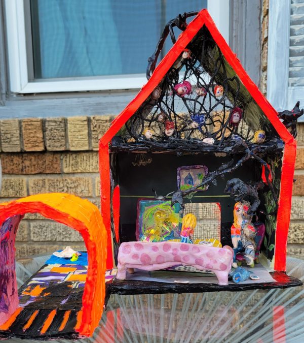 paper mache art house that is neon orange has faces in the attic and living room on the ground floor