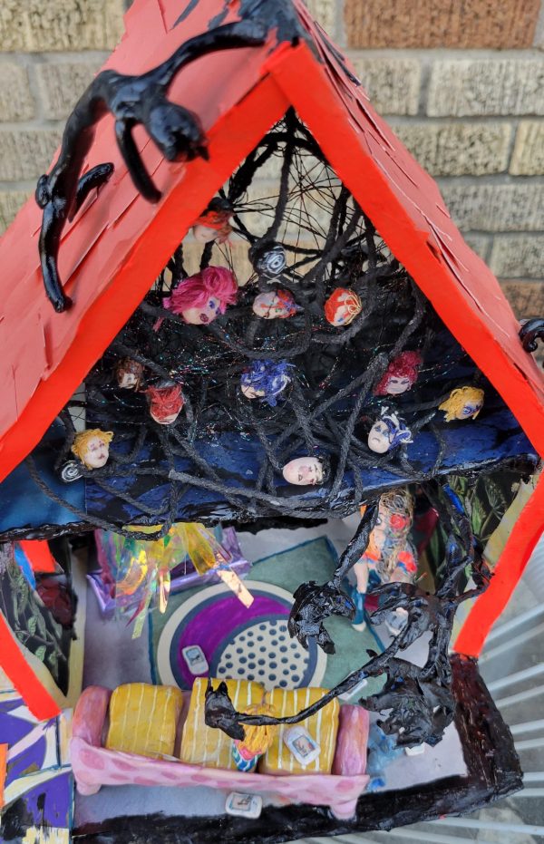 paper mache art house that is neon orange has faces in the attic and living room on the ground floor